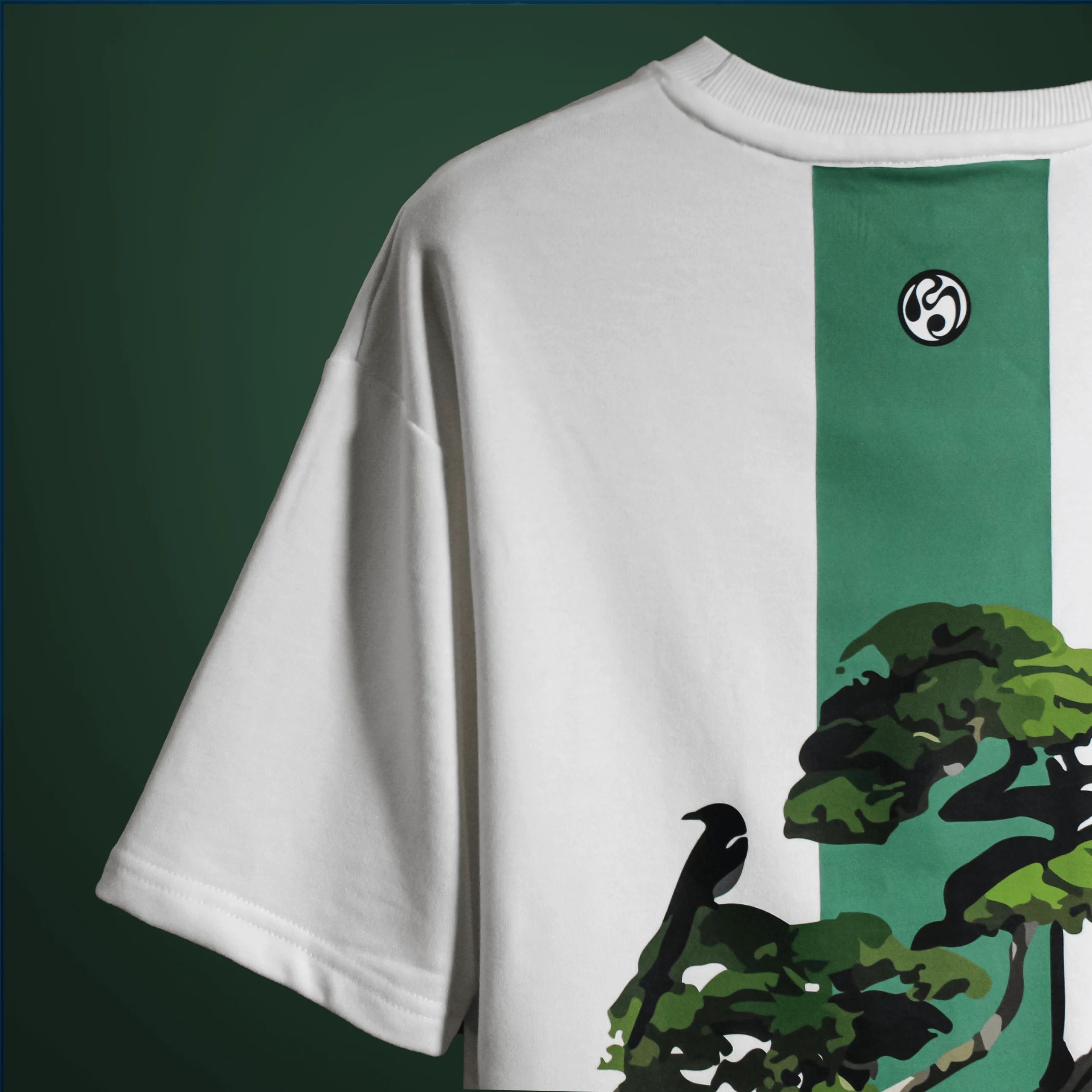 Back view of the Bonsai Tree T-Shirt showing a green vertical stripe with an artistic bonsai tree and crow graphic, printed on white fabric.