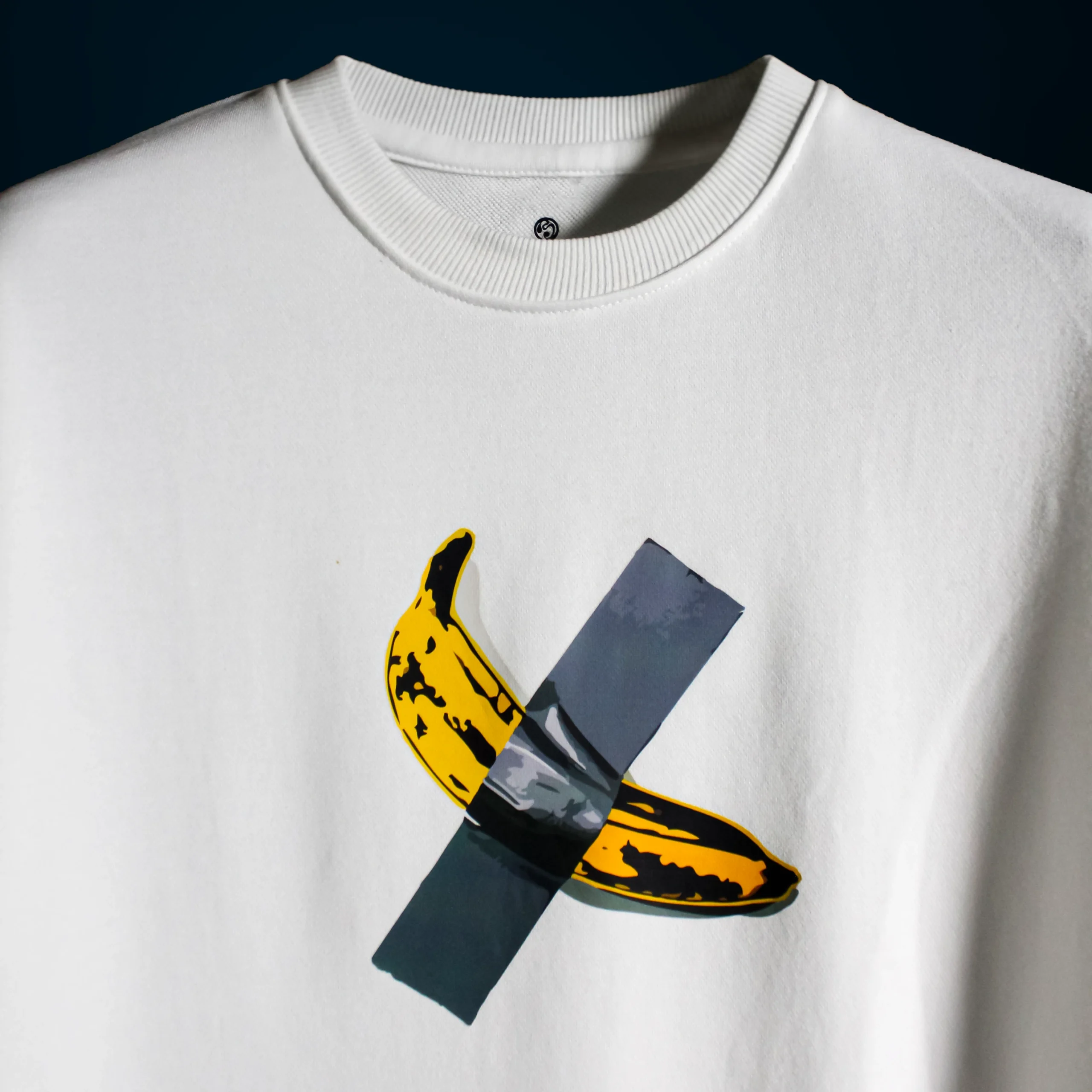 Close-up of the $6 Million Banana T-Shirt featuring a duct-taped banana graphic on white cotton fabric near the neckline.