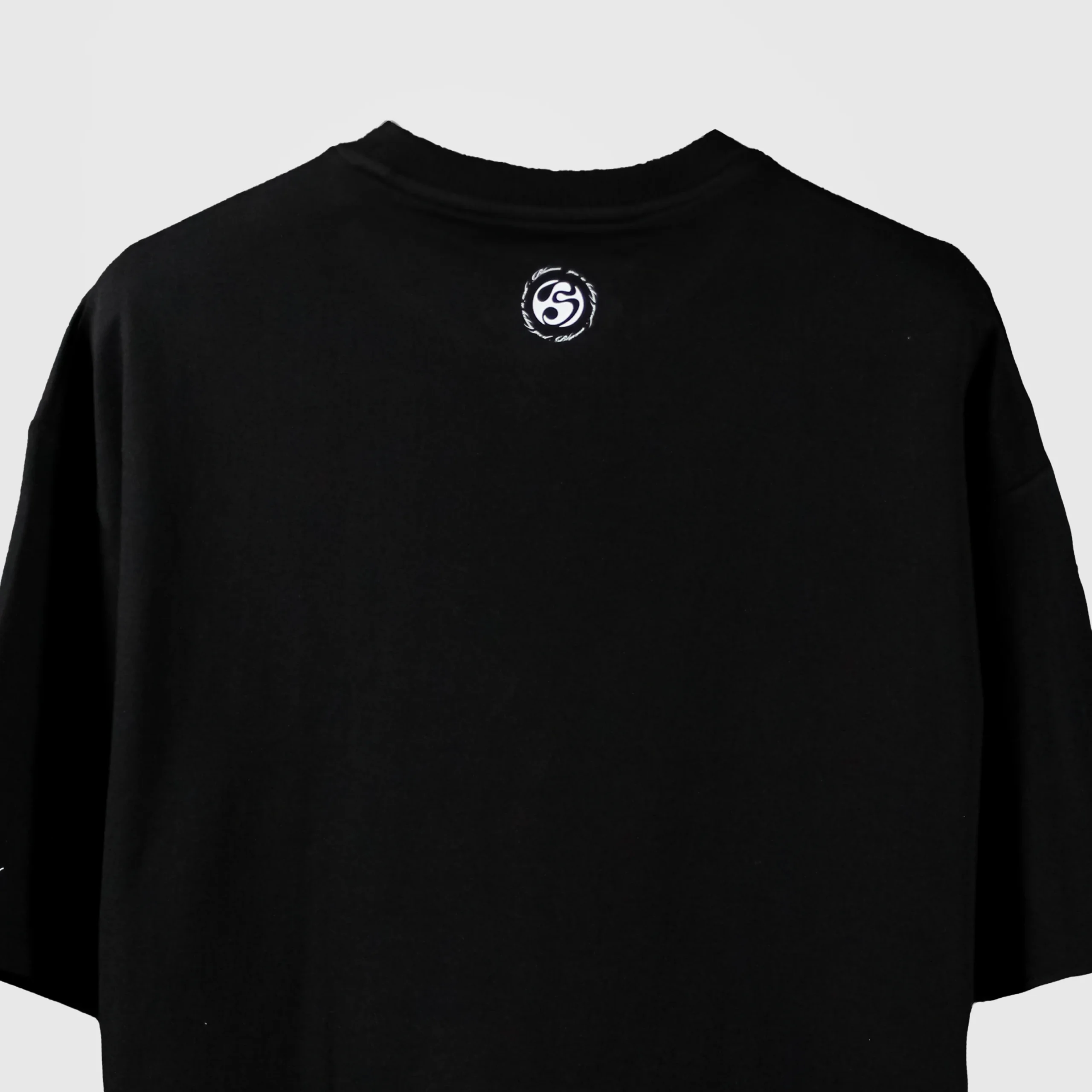 Back view of black oversized t-shirt with small circular Blumun logo printed below the collar – minimalist streetwear branding