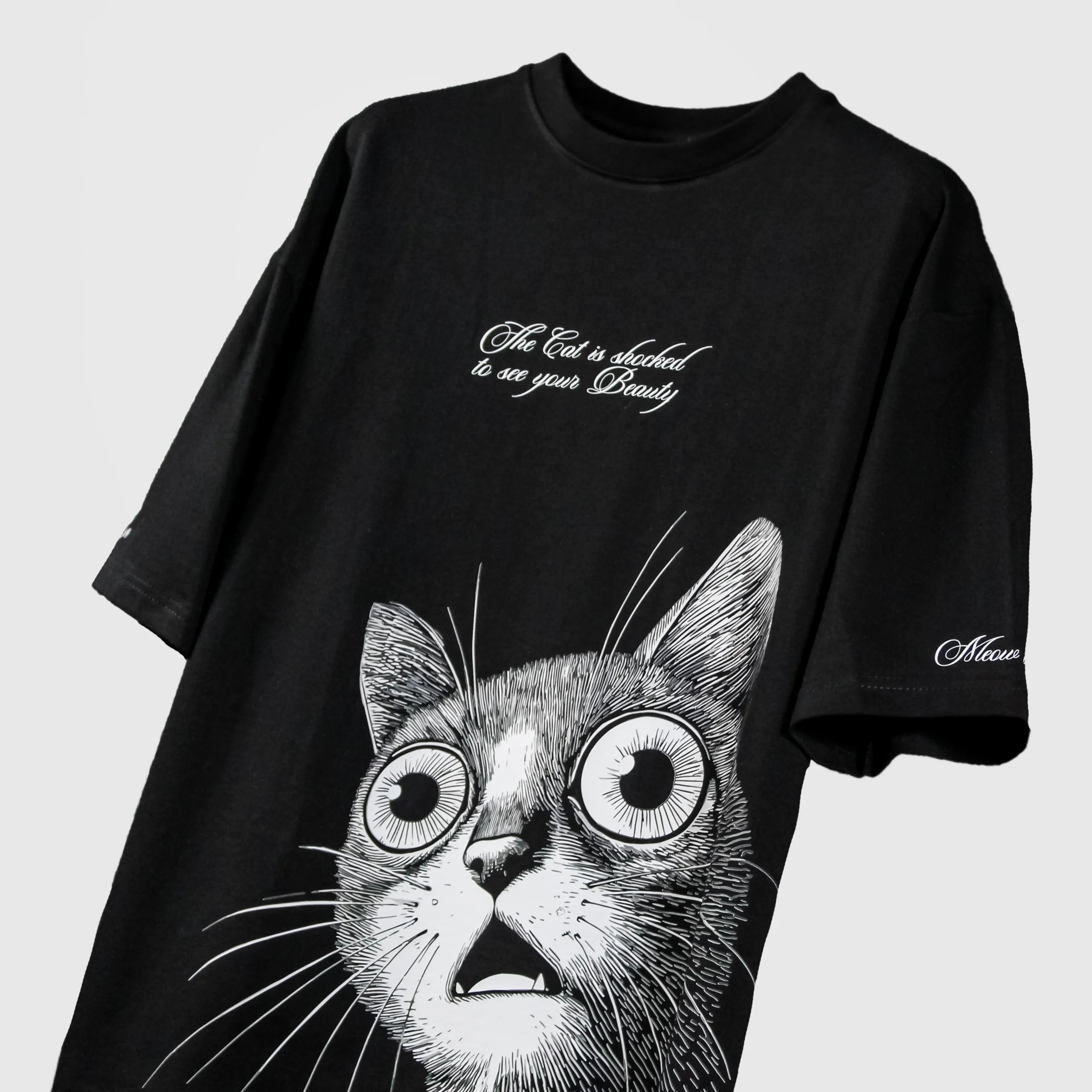 Black oversized streetwear t-shirt with large shocked cat graphic and 'The Cat is shocked to see your Beauty' text on front – bold monochrome illustration with Meow branding on sleeve